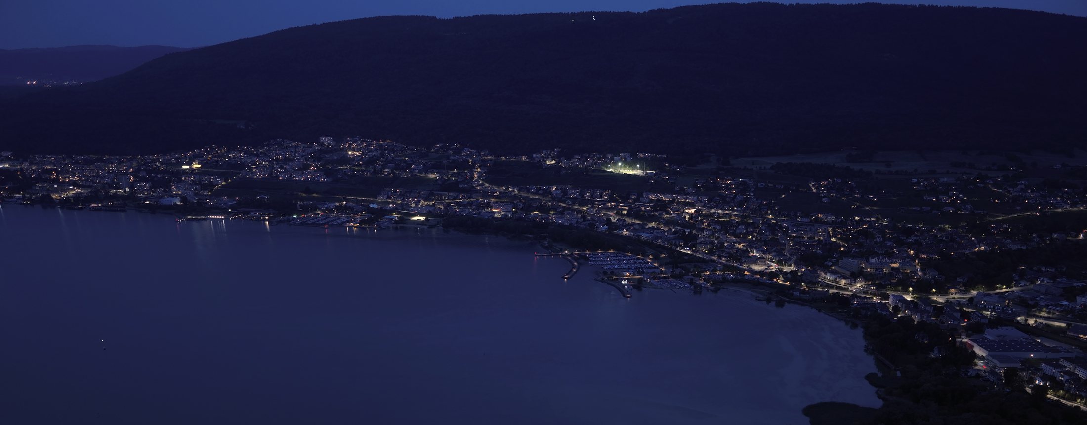 Vue aérienne nocturne de la commune de Laténa, au bord du lac de Neuchâtel, éclairage public allumé.
